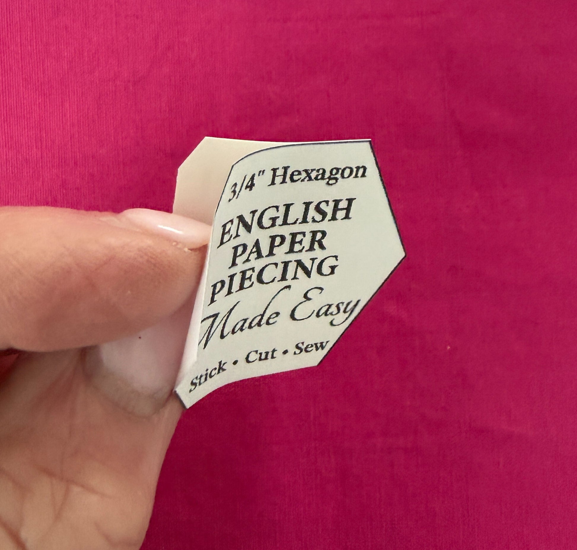 Hexagonal paper piecing template held over a pink fabric background peel paper backing off