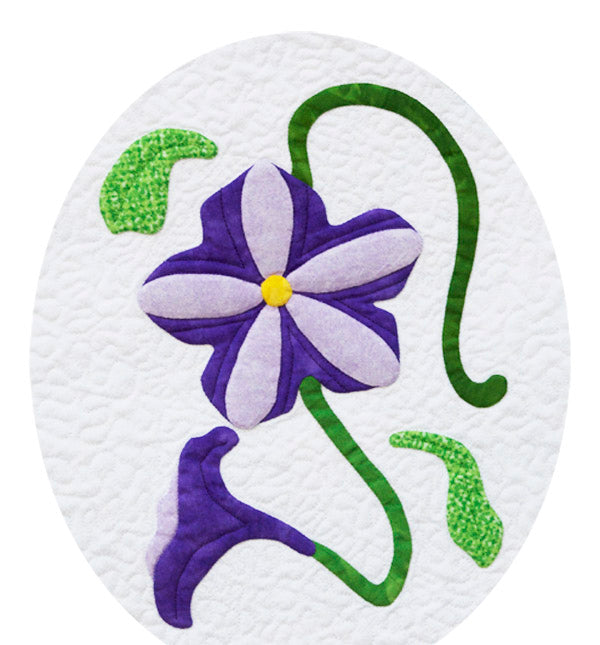 A quilted petunia flower pattern with a purple center and green leaves on a white background, showcasing the appliqué technique.
